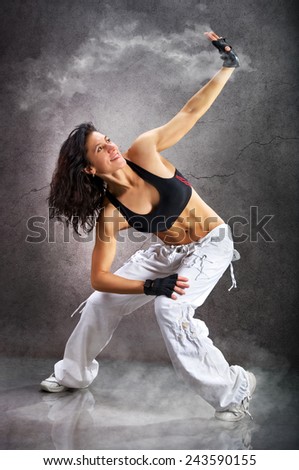 Young beautiful athletic woman dancing modern dance hip-hop on wall background with smoke