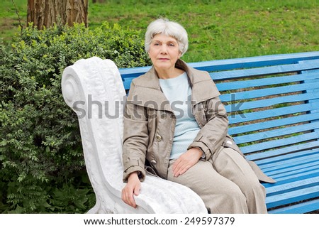 beautiful cute elderly woman sitting on a park bench blue