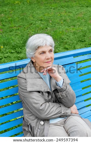 beautiful cute elderly woman sitting on a park bench blue