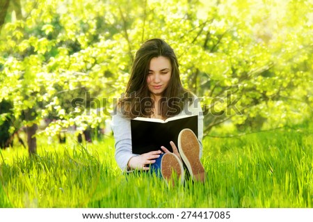beautiful young  woman reading a book in the park sitting on the grass in a sunny meadow
