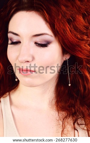 Beautiful young redhead woman with perfect daytime makeup and long silver earrings smiling playfully