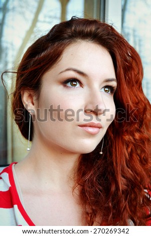 Beautiful young redhead woman with perfect daytime makeup and long silver earrings smiling playfully