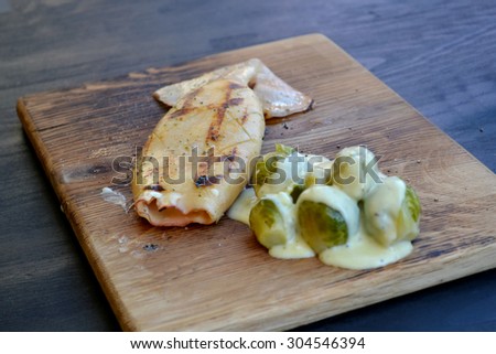 Grilled calamari with Brussels sprouts covered in sauce on wooden board