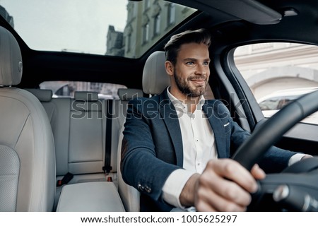 Success in motion. Handsome young man in full suit smiling while driving a car Foto stock © 