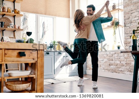 Romance. Full length of beautiful young couple in casual clothing dancing and smiling while standing in the kitchen at home