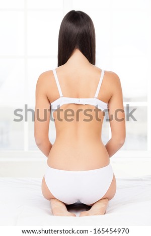 Woman in lingerie. Rear view of young woman in lingerie kneeling on the bed
