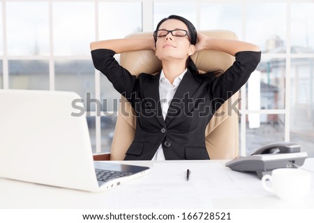 Chill time. Cheerful young business woman holding head in hands and keeping eyes closed while sitting at her working place