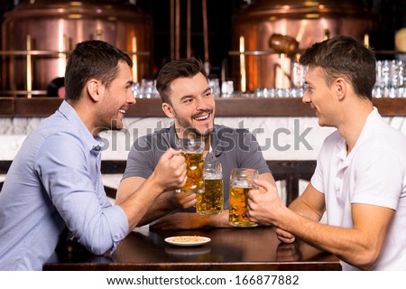 Spending time in bar. Three cheerful friends drinking beer in bar