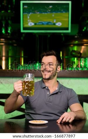 Man in beer pub. Cheerful young man holding a mug with beer and smiling while sitting in bar