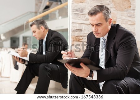 Businessman making notes. Confident mature man in formalwear making notes in his note pad while sitting on staircase