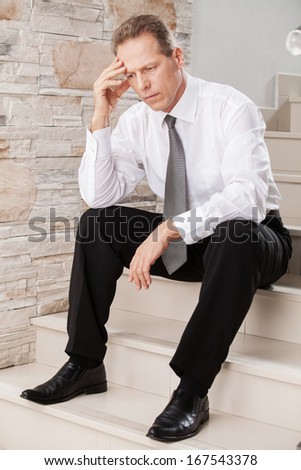 Depressed businessman. Depressed mature man in formalwear holding head in hand while sitting on staircase