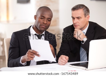Discussing a project. Two confident business people in formalwear discussing something while one of them pointing a paper