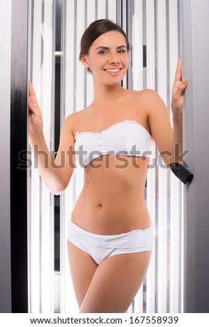 Beautiful woman in solarium. Attractive young woman standing in tanning booth and smiling