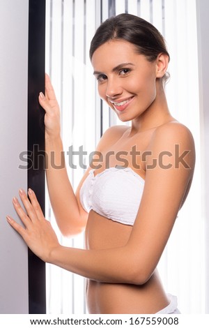 Beauty in solarium. Beautiful young woman standing in tanning booth and smiling at camera