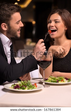 It is delicious! Beautiful young couple feeding each other and smiling while spending time at the restaurant