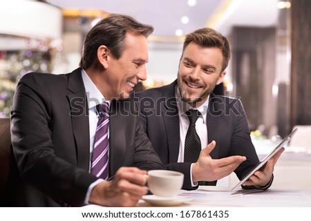 Successful project. Two cheerful business people in formalwear discussing something and smiling while one of them pointing digital tablet