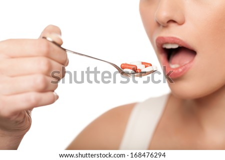 Woman taking pills. Cropped image of young woman holding a spoon full of pills and keeping mouth open while isolated on white