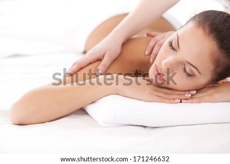 Total relaxation. Beautiful young woman lying on front and looking at camera while massage therapist massaging her shoulders