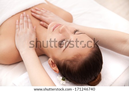 Enjoying massage at spa. Top view of beautiful young woman lying on back and keeping her eyes closed while massage therapist massaging her
