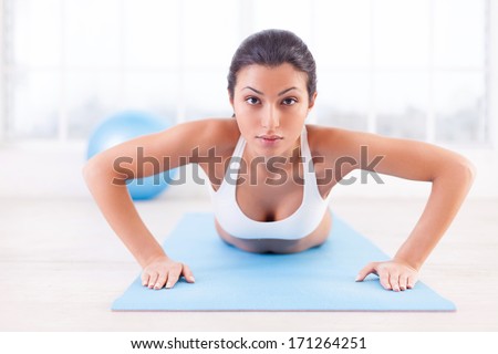 Woman exercising. Confident young Indian woman training on yoga mat and looking at camera