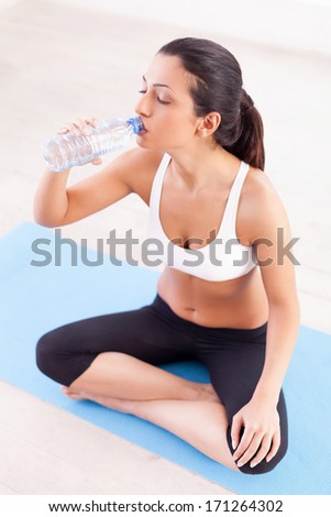 Staying refreshed. Top view of attractive young Indian woman sitting in lotus position and drinking water