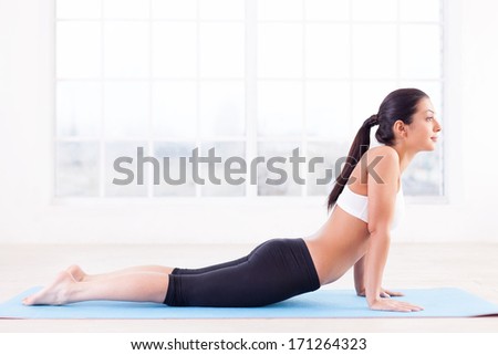 Working out. Side view of beautiful young Indian woman training on yoga mat