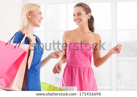 Enjoying shopping. Two cheerful young women in dresses walking together and holding shopping bags