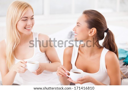 Spending time together. Two attractive young women sitting on bed together and drinking coffee