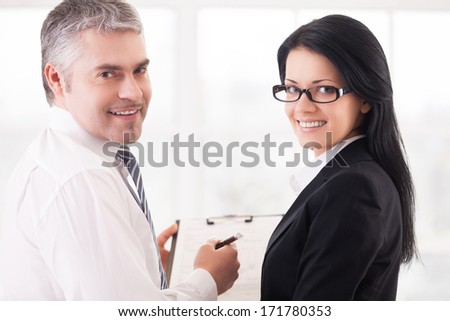Business people doing paperwork. Two smiling business people writing something in note pad and looking over shoulder