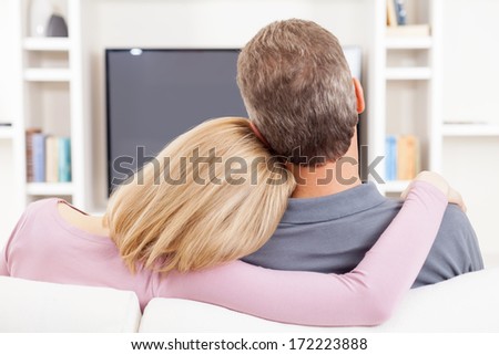 Couple watching TV. Rear view of mature couple sitting in front of TV while woman hugging her husband