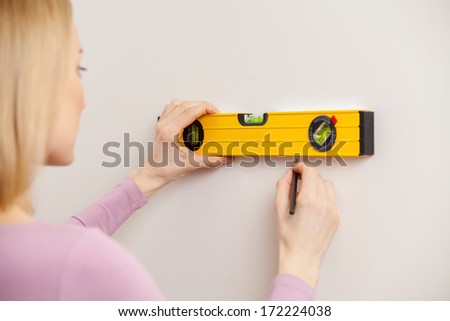 Woman with measuring tape. Rear view of blond hair woman taking measurements of the wall
