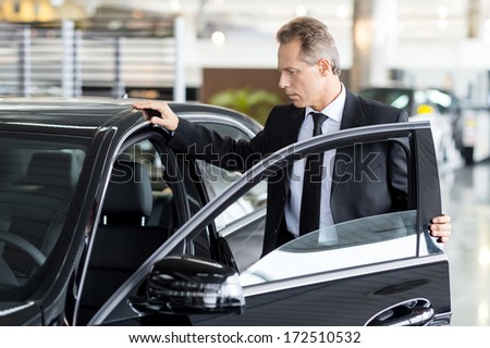 Examining his new car. Confident mature man in formalwear opening the car door at the dealership