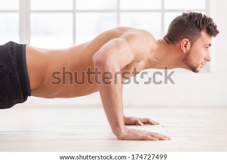 Push-ups. Side view of young muscular man doing push-ups and looking away