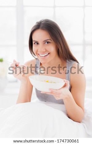 Having a breakfast in bed. Cheerful young smiling woman having a breakfast in bed and smiling at camera