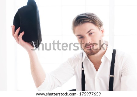 Nice to meet you! Handsome young man in shirt and suspenders holding a hat near head and looking at camera with smile