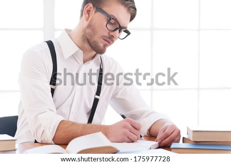 Author at work. Confident young man in shirt and suspenders writing something in note pad while sitting at his working place