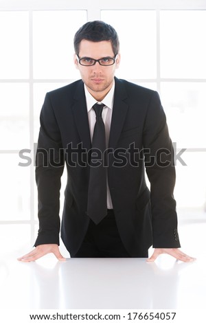 Confident businessman. Confident young man in formalwear looking at camera while leaning at the table
