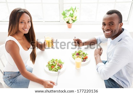 Having a healthy breakfast. Top view of beautiful young African couple sitting together at the table and eating salads with orange juice