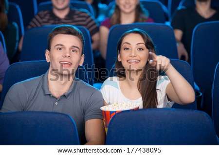 Couple at the cinema. Happy young couple eating popcorn and drinking soda while watching movie at the cinema