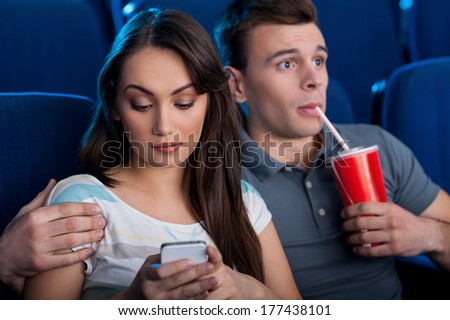 What an exciting movie! Excited young couple eating popcorn and drinking soda while watching movie at the cinema