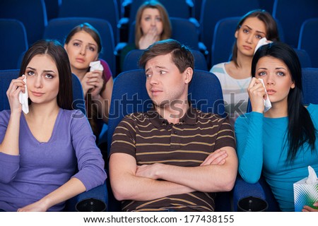 This movie is for ladies only. Young man sitting together with crying women while watching movie at the cinema