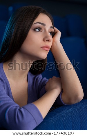 Beauty at the cinema. Attractive young woman holding head in hand while watching movie at the cinema