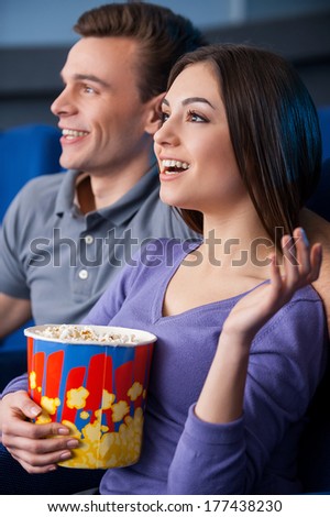 What an exciting movie! Side view of happy young couple eating popcorn while watching movie at the cinema