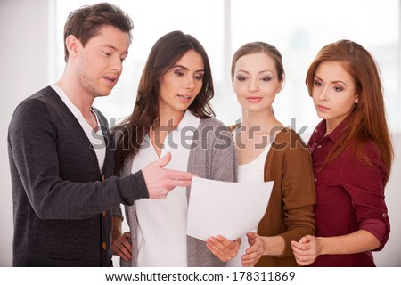 Discussing a contract. Group of young people discussing document while standing close to each other
