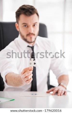 Be a part of our team! Confident young man in shirt and tie showing the last element from puzzle while sitting at his working place