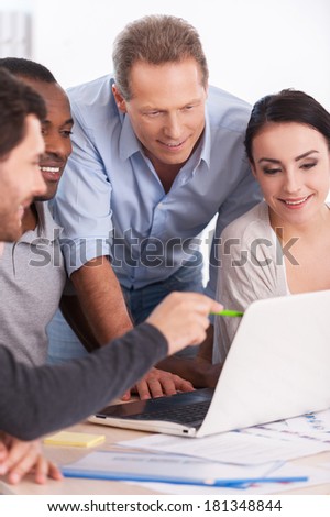 Creative team brainstorming. Group of business people in casual wear sitting together at the table and discussing something while looking at the laptop