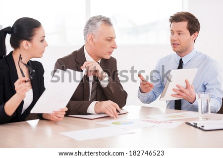 Presenting his ideas. Three confident business people discussing something while sitting at the table