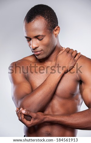 Feeling pain in elbow. Young muscular African man touching his elbow while standing against grey background