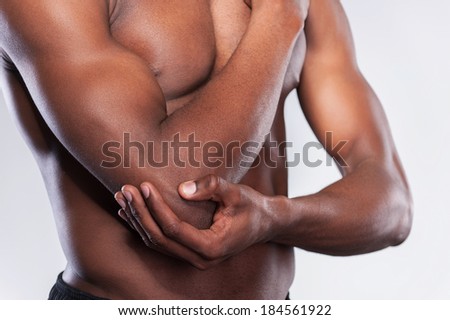 Pain in elbow. Cropped image of young muscular African man touching his elbow while standing against grey background