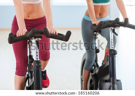Girls on exercise bikes. Cropped image of two young women in sports clothing exercising on gym bicycles